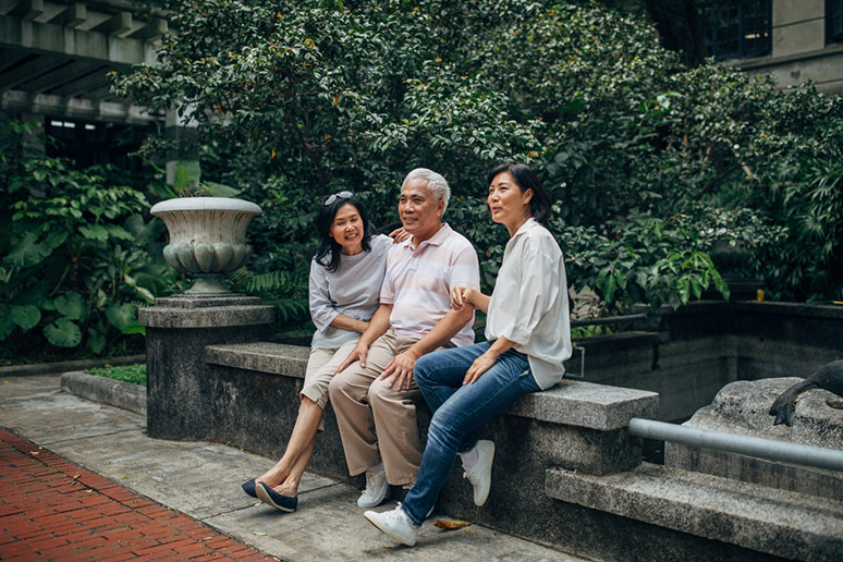 Two ladies sitting with elderly father on a bench