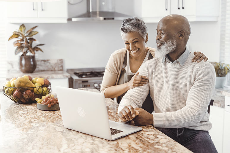 Happy senior couple browsing on he computer in their kitchen at home